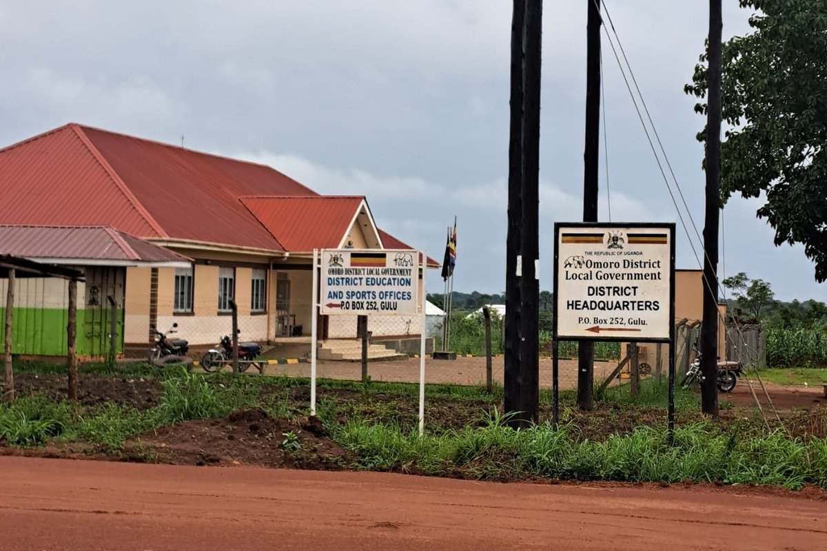 Roadside signs for the Omoro District Local Government headquarters and the District Education and Sports Offices, next to a dirt road in northern Uganda